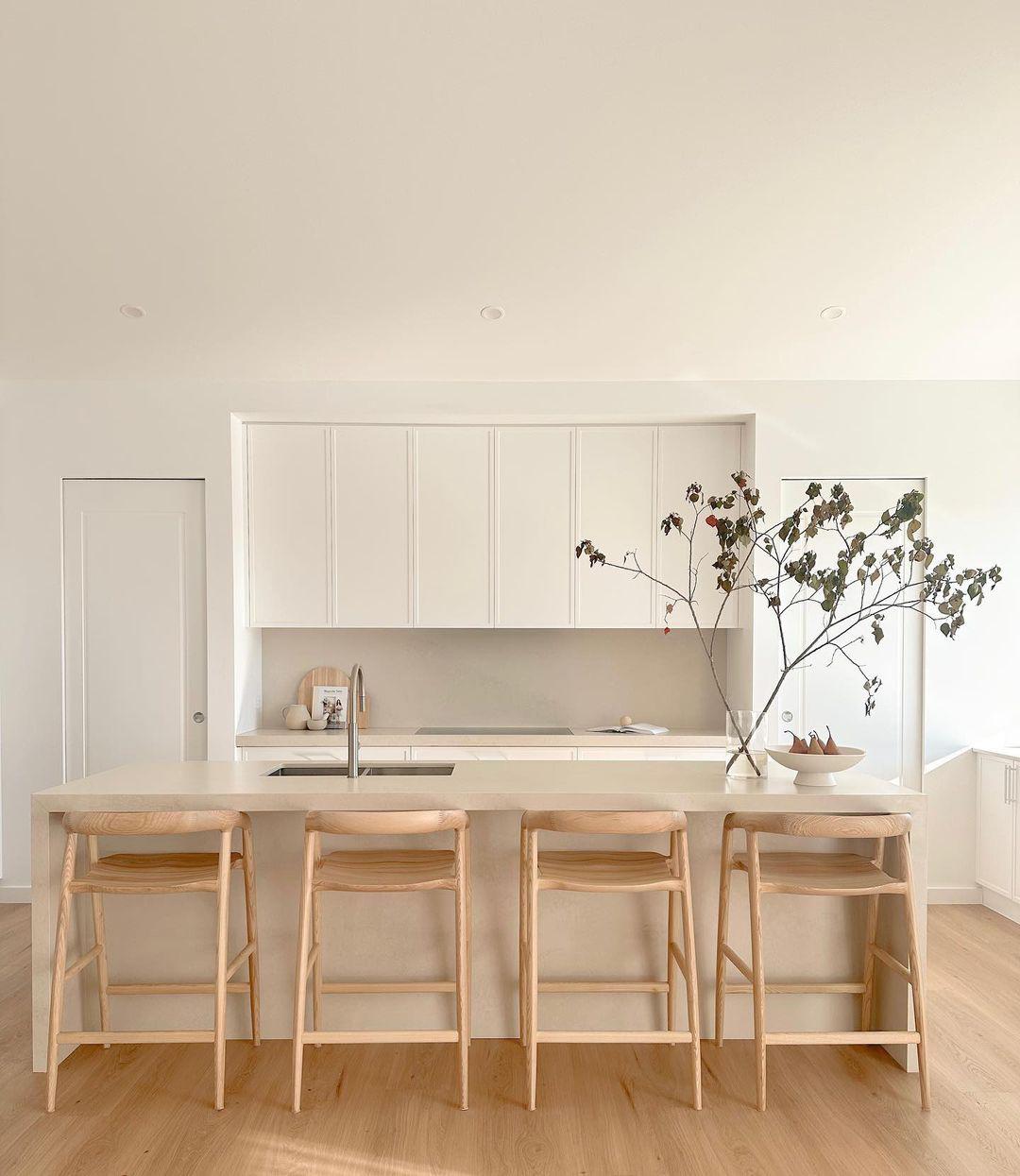 Light kitchen with white cabinetry, a stone island and four timber stools